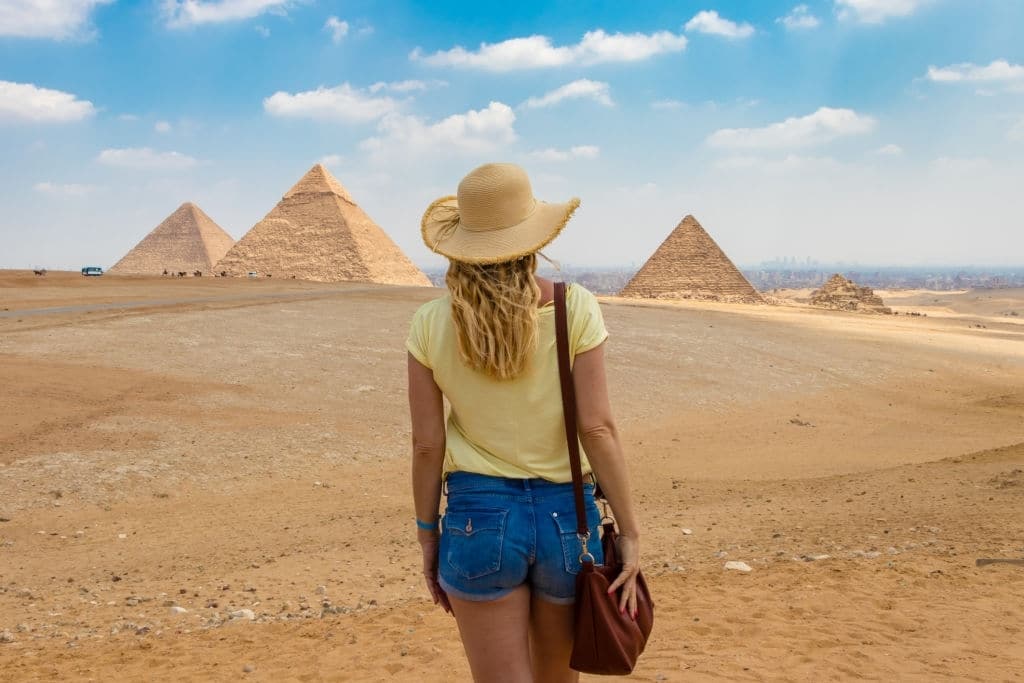 Egypt Packages - Young girl in the desert. Back view portrait of a single woman watching the Great Pyramids of Giza in Egypt