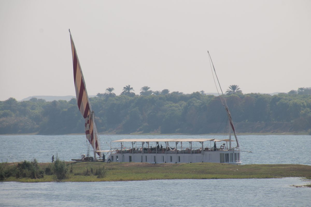 Don't Take Our Word For It - 11 - EZ TOUR EGYPT A dahabiya moored against a green Nile bank with its striped sail furled and guests on the shaded upper deck